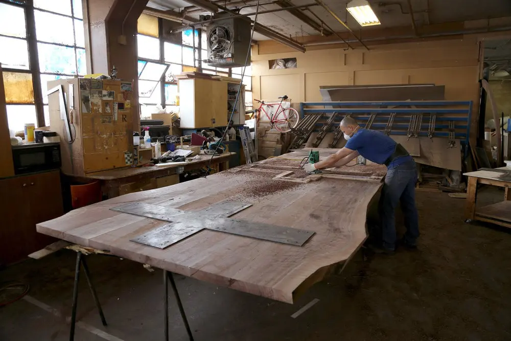 SentienMaking the table ready to attached the legs Woodworker working on extra large SENTIENT American Black Walnut Signature Live Edge Table.t High-end commercial furniture in production