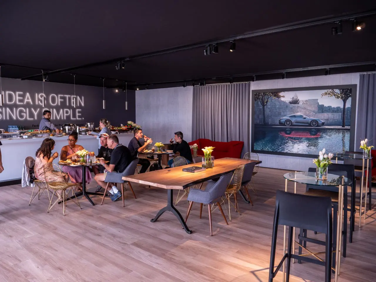 a luxury SENTIENT contemporary designed walnut raw edge dining table in Porsche car show exhibition café with people sitting