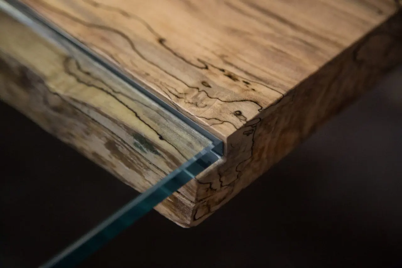 a SENTIENT contemporary designed Colorado ambrosia table in maple with custom glass inset and blackened steel v shape leg