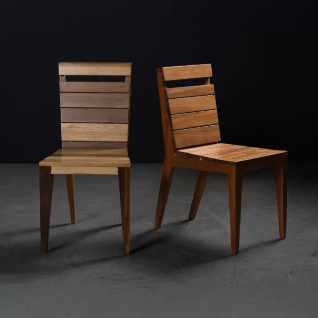 A pair of SENTIENT Angle Chairs showcasing sleek designs, one crafted from mixed hardwoods and the other from rich walnut. The chairs feature slatted backs and minimalist aesthetics, perfect for modern interiors.