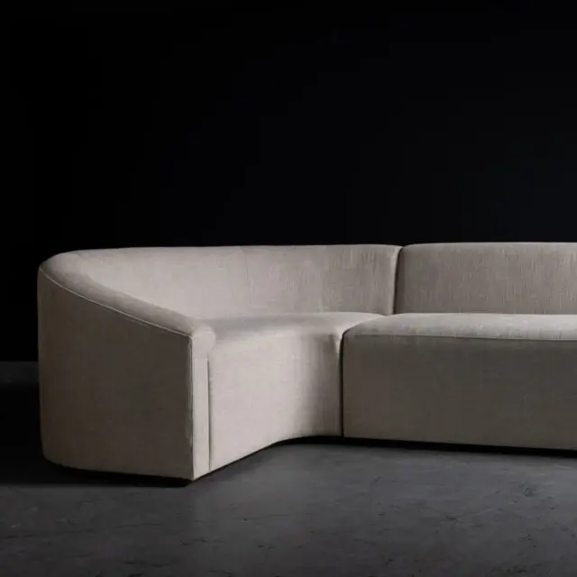 The SENTIENT Baashe Sofa featuring a modern curved design and upholstered in a neutral fabric. The sleek and minimalist aesthetic provides a sophisticated seating solution for contemporary interiors.