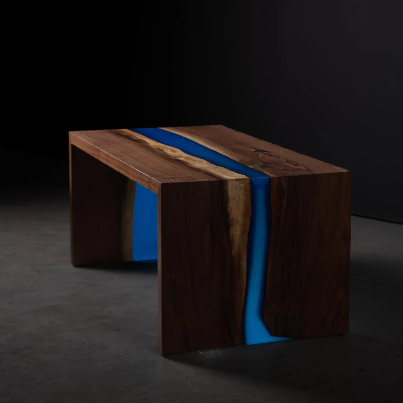 A striking SENTIENT Epoxy River Table crafted from black walnut, featuring a vibrant blue resin river running through its center. The table showcases a seamless blend of natural wood and modern resin artistry.