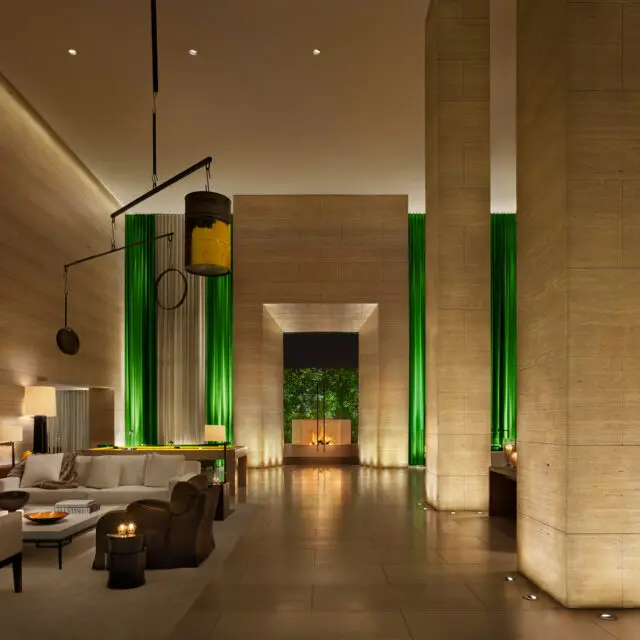 A luxury hotel interior featuring custom furniture by SENTIENT, with high ceilings, illuminated green drapes, and a warm, modern aesthetic. The design highlights the harmonious blend of bespoke furniture and architectural elegance.