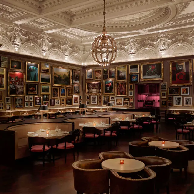 An opulent restaurant interior featuring SENTIENT custom seating and tables, surrounded by an ornate ceiling and a gallery wall of framed artwork. The space exudes sophistication and elegance, blending fine dining with artistic ambiance.