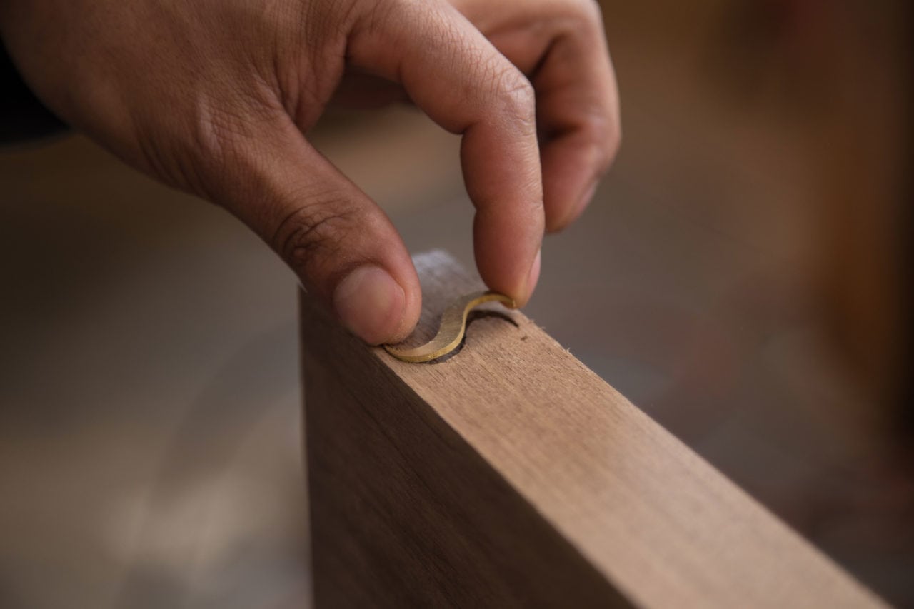 a hand setting a brass letter S into the end of a contemporary walnut wood slab 