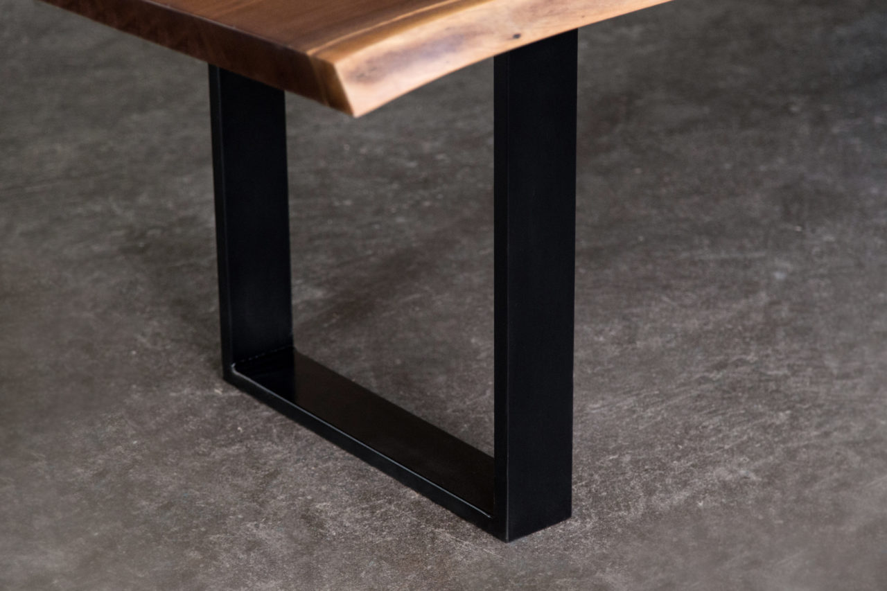 a corner detail of a SENTIENT American black walnut luxury lived edge table with blackened steel square frame leg