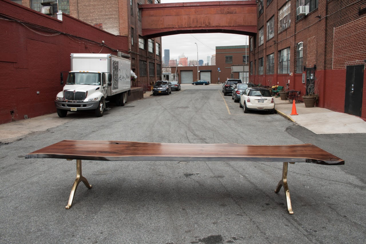 a luxury live edge SENTIENT contemporary designed custom table with brass wishbone legs outside amongst parked cars