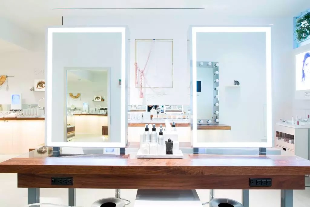 in an honest beauty retail space SENTIENT contemporary designed custom walnut counter top with two mirrors and beauty aids 