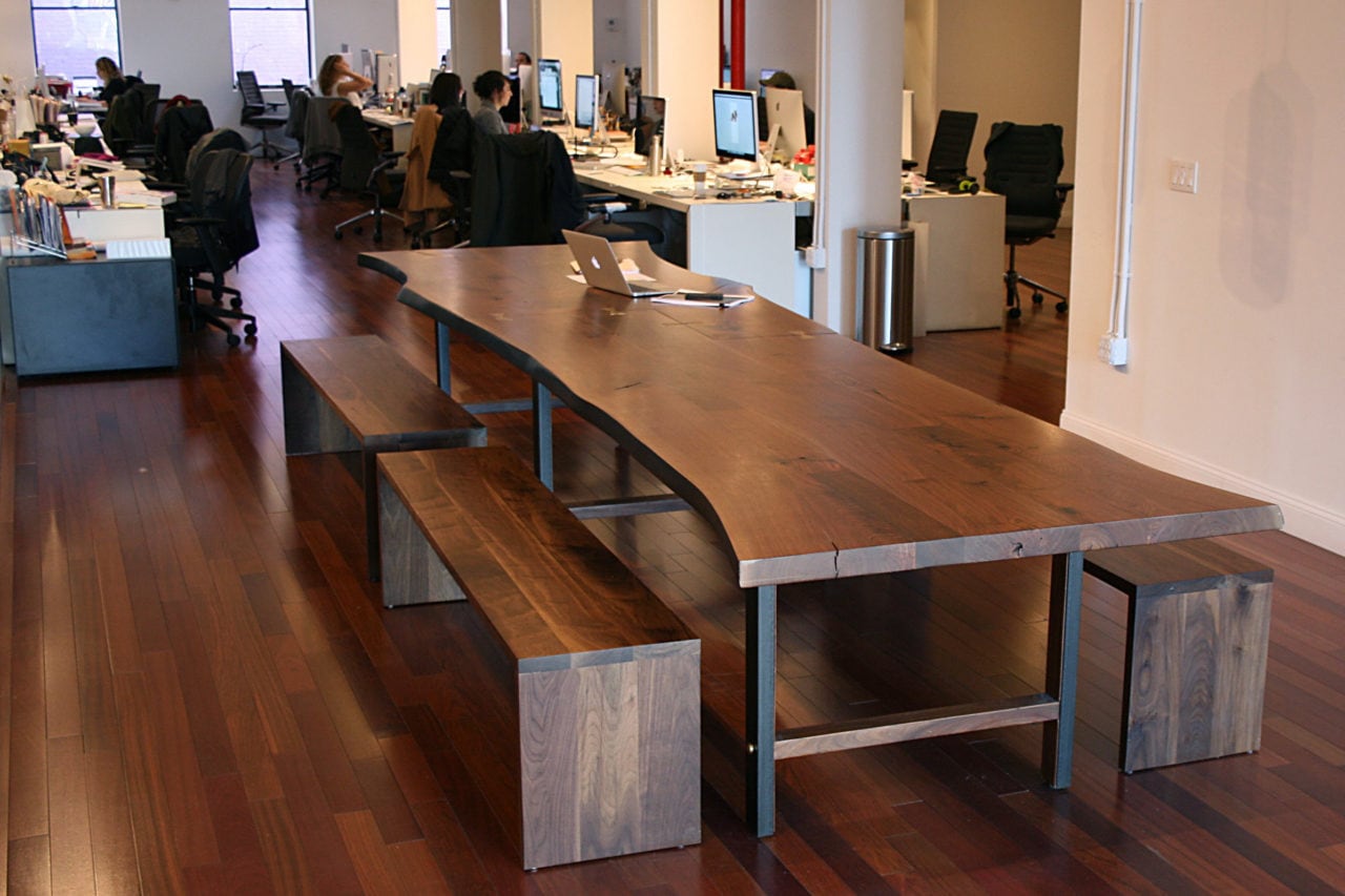A SENTIENT contemporary live edge custom walnut table with benches in an open office setting