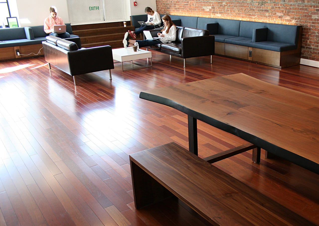 A SENTIENT contemporary live edge custom walnut table with benches in an office setting with people sitting on a custom banquette 