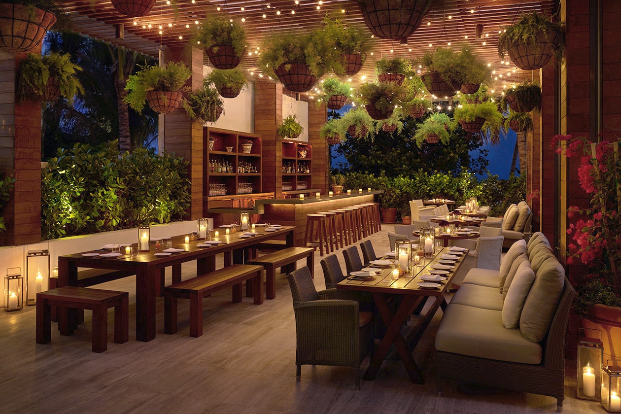 an outdoor covered patio bar setting with plants and SENTIENT contemporary designed communal tables at a Miami edition hotel