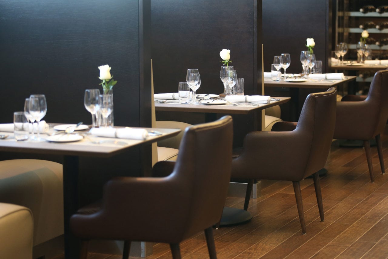 a row of custom SENTIENT walnut contemporary tables and chairs divided by black walls in British airways restaurant
