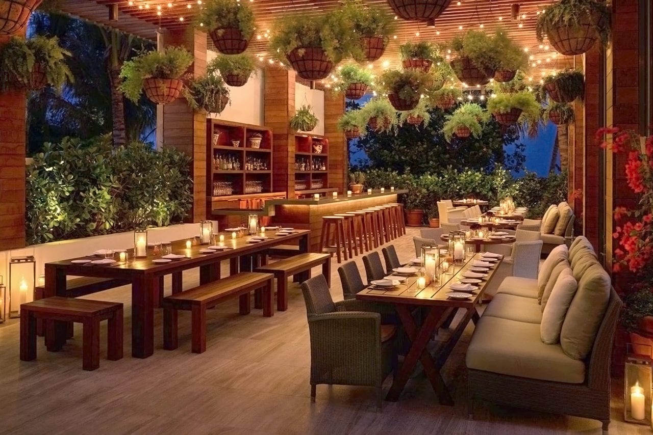 an outdoor covered patio bar setting with plants and SENTIENT contemporary designed communal tables at a Miami edition hotel