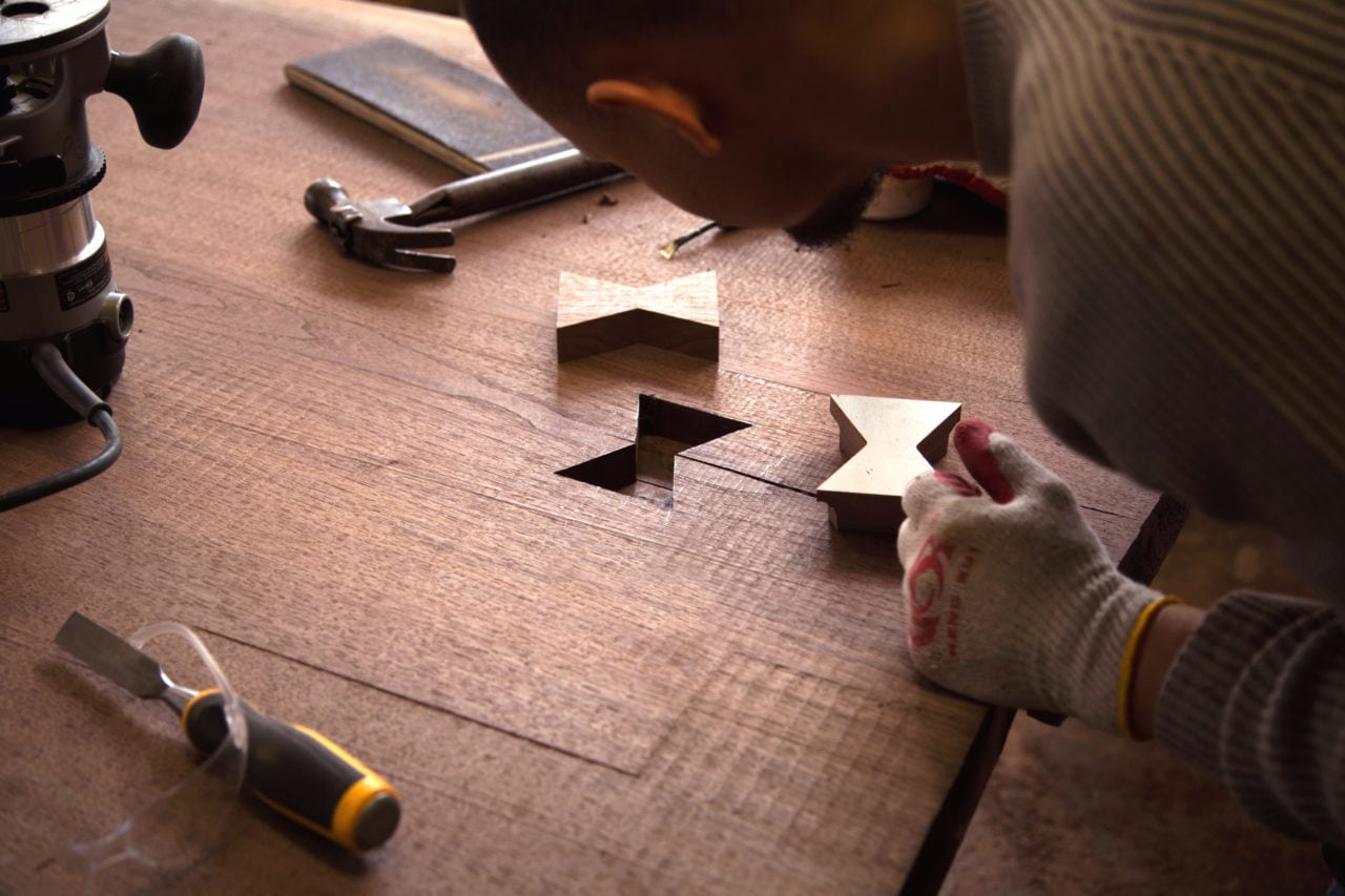 a man in SENTIENT workshop setting a contemporary designed brass butterfly joint into wood custom slab