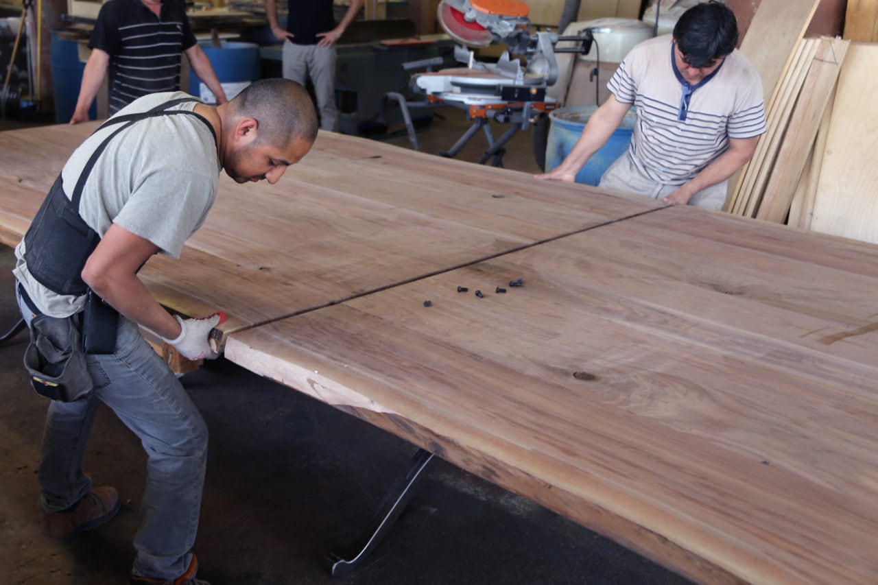 several men putting together a SENTIENT designed custom table using two large walnut wood slabs