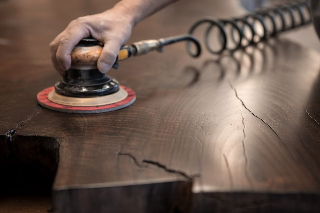 A close up of a hand sanding a SENTIENT contemporary designed wooden custom table