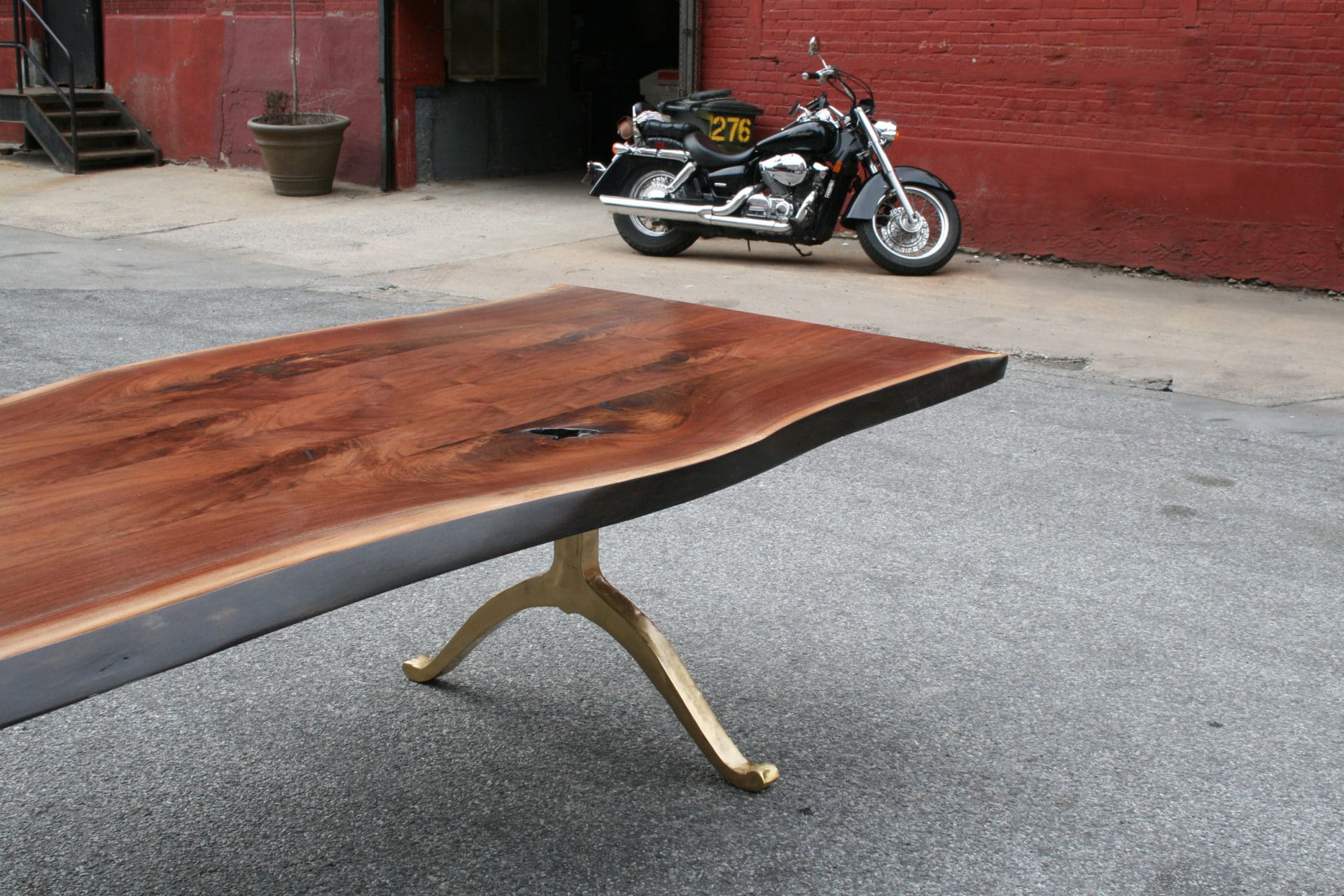 a SENTIENT designed walnut custom live edge luxury table with brushed brass wishbone legs outside with motorcycle 