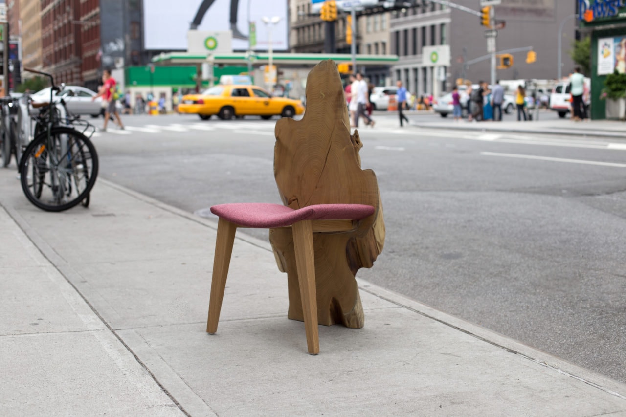 a contemporary designed SENTIENT locust dining chair with live edge wood back and curved luxury upholstered seat on sidewalk