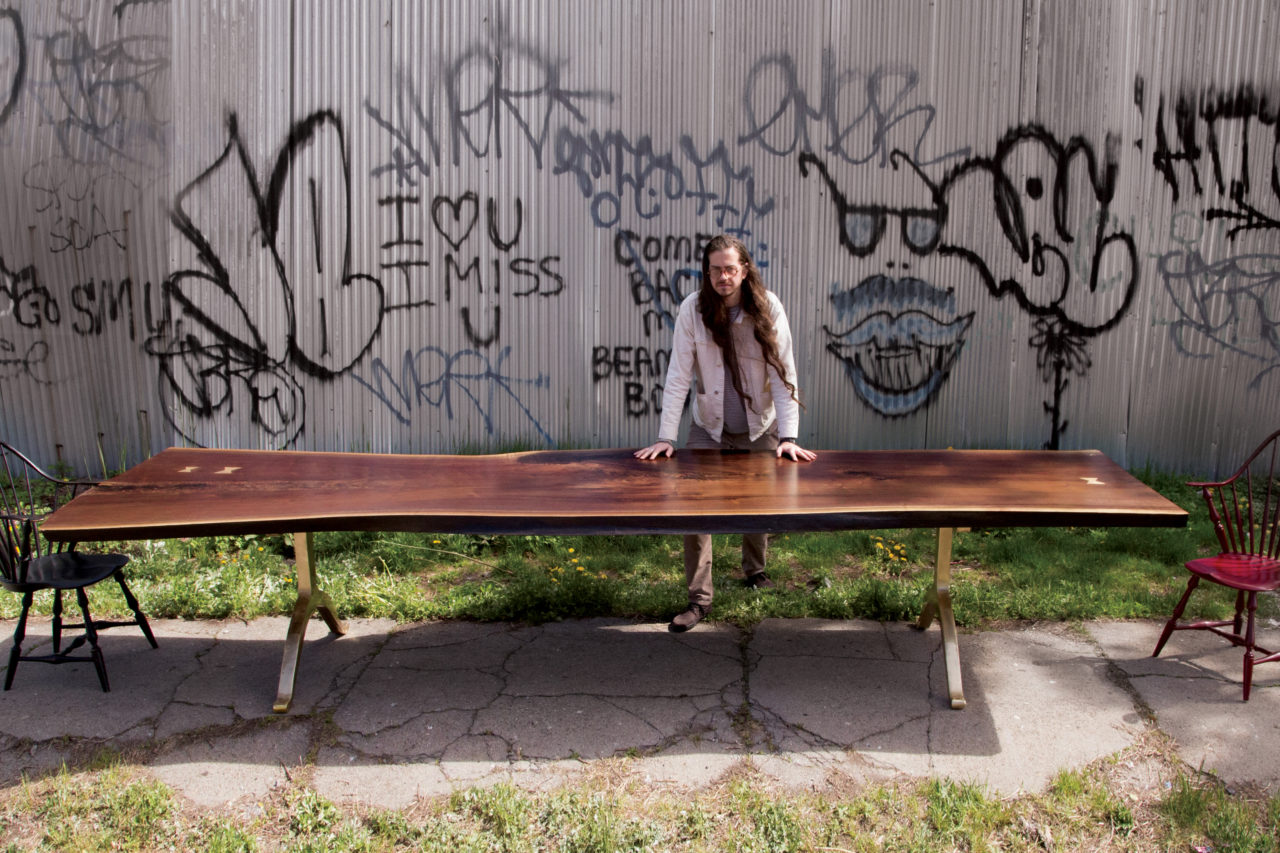 man behind a live edge walnut conference table in front of a graffitied wall