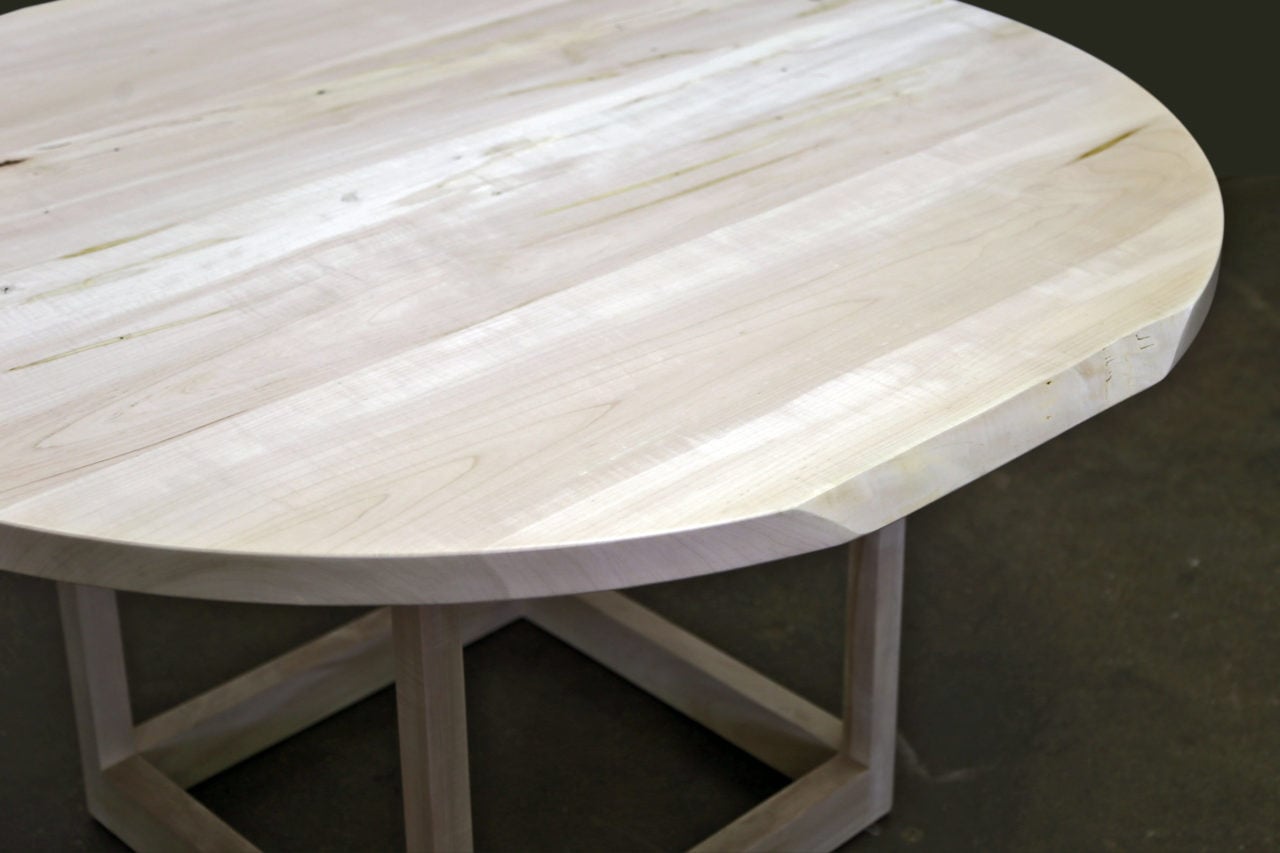 a SENTIENT contemporary designed round Flow pedestal table in light stained luxury maple wood with partial live edge