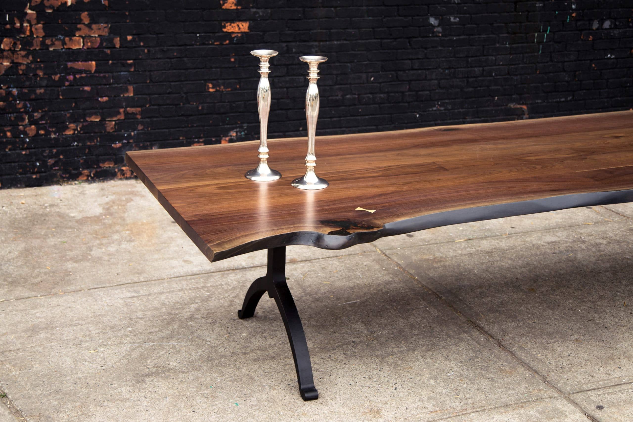a SENTIENT American black walnut live edge table with blackened steel legs with two silver candlesticks on top