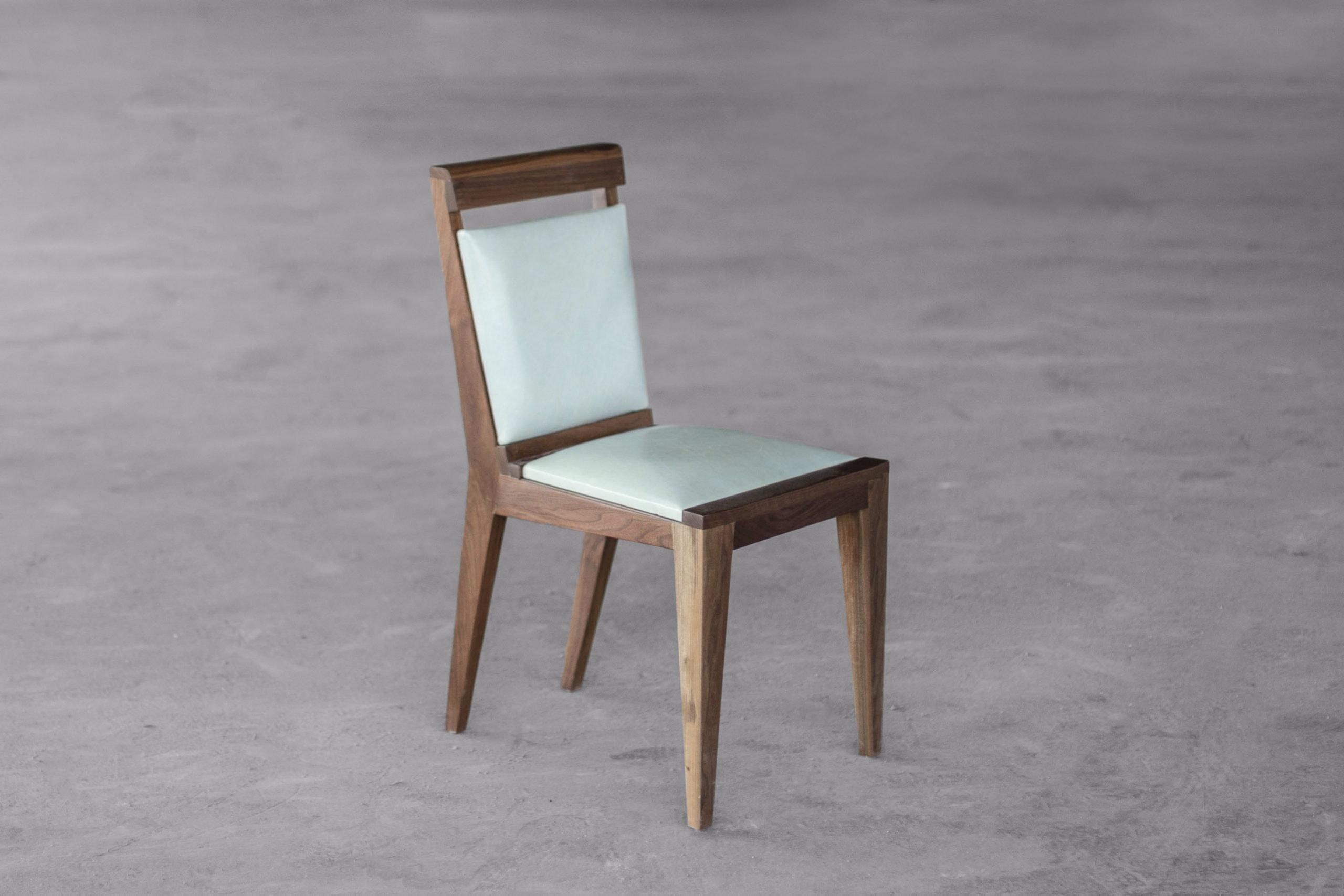 SENTIENT contemporary designed Angles dining chair in walnut with custom turquoise color leather upholstery on a concrete floor