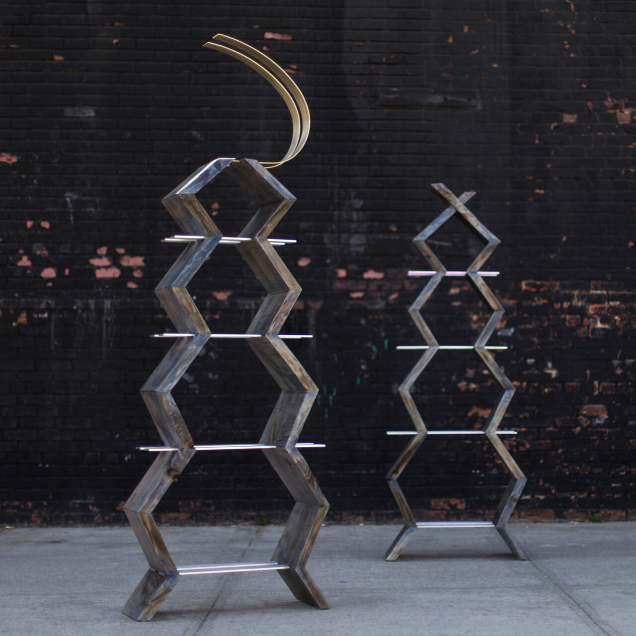 SENTIENT's Friends Concept, and artistic shelving unit with a series of stacked geometric walnut blocks, intersected by thin glass shelves, against a textured black brick wall.