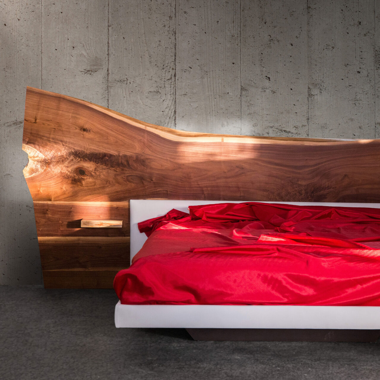 A SENTIENT Furniture crafted live-edge bed with a natural walnut headboard and a stark, white frame, highlighted by vibrant red bedding.