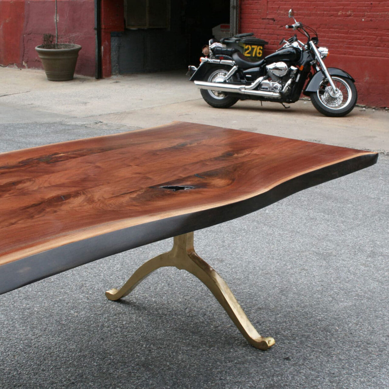 Luxury live edge table, with brass wishbone legs, photographed in front of a motorcycle, on the streets of Brooklyn, New York