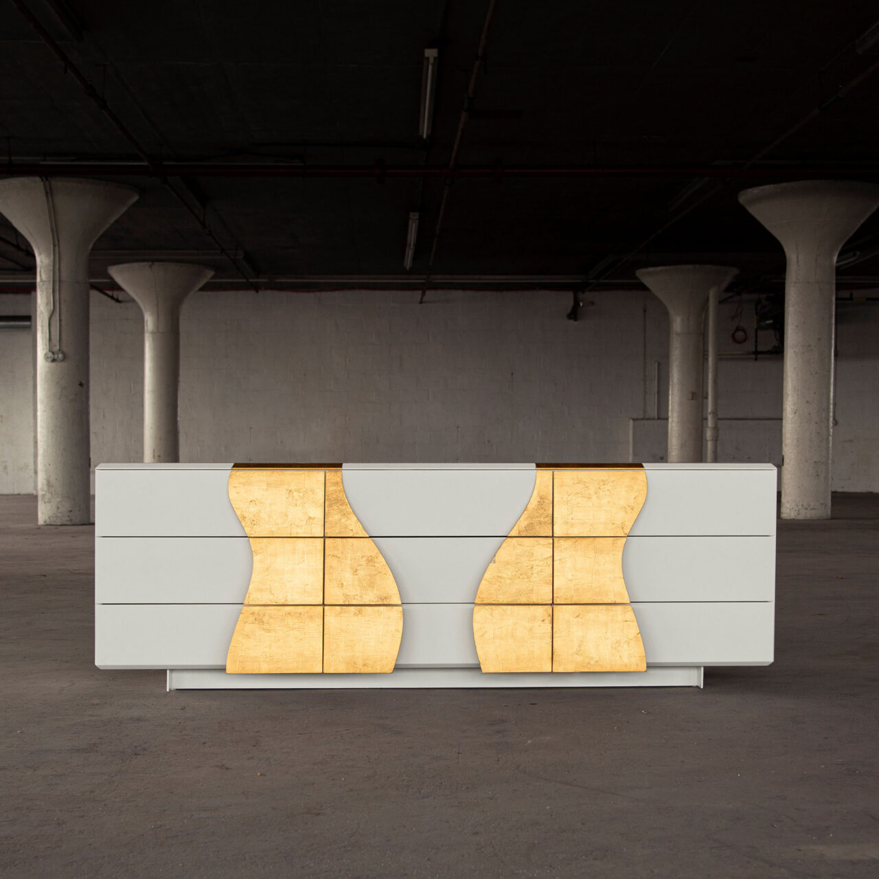 A SENTIENT melodious dresser featuring a clean, white finish with unique, wave-like wood grain drawer fronts in a concrete floored room.