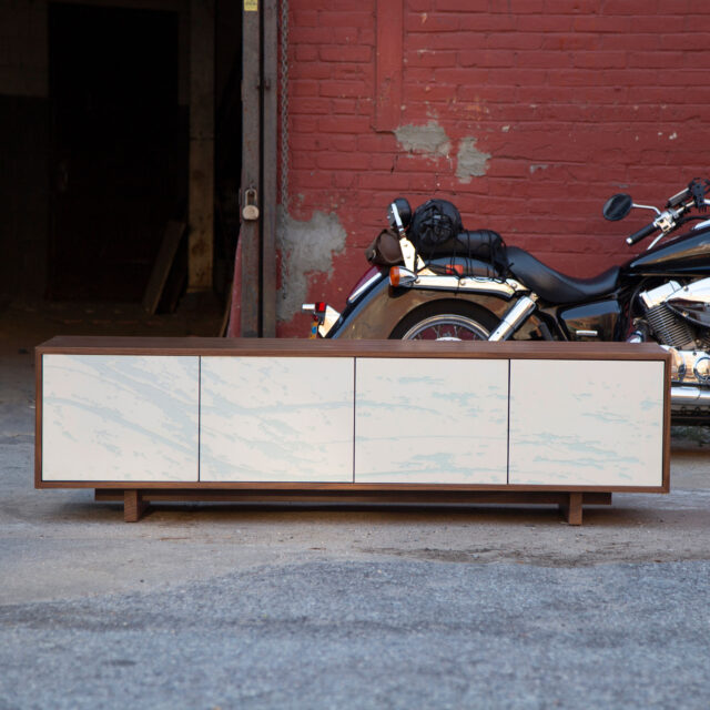 Elegant SENTIENT Neesho credenza with a smooth, light grey surface and natural wood accents, presented in an urban, open-concept area.