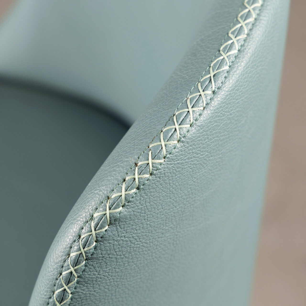 Close up of cross stitches of a custom chair upholstered in sage green leather