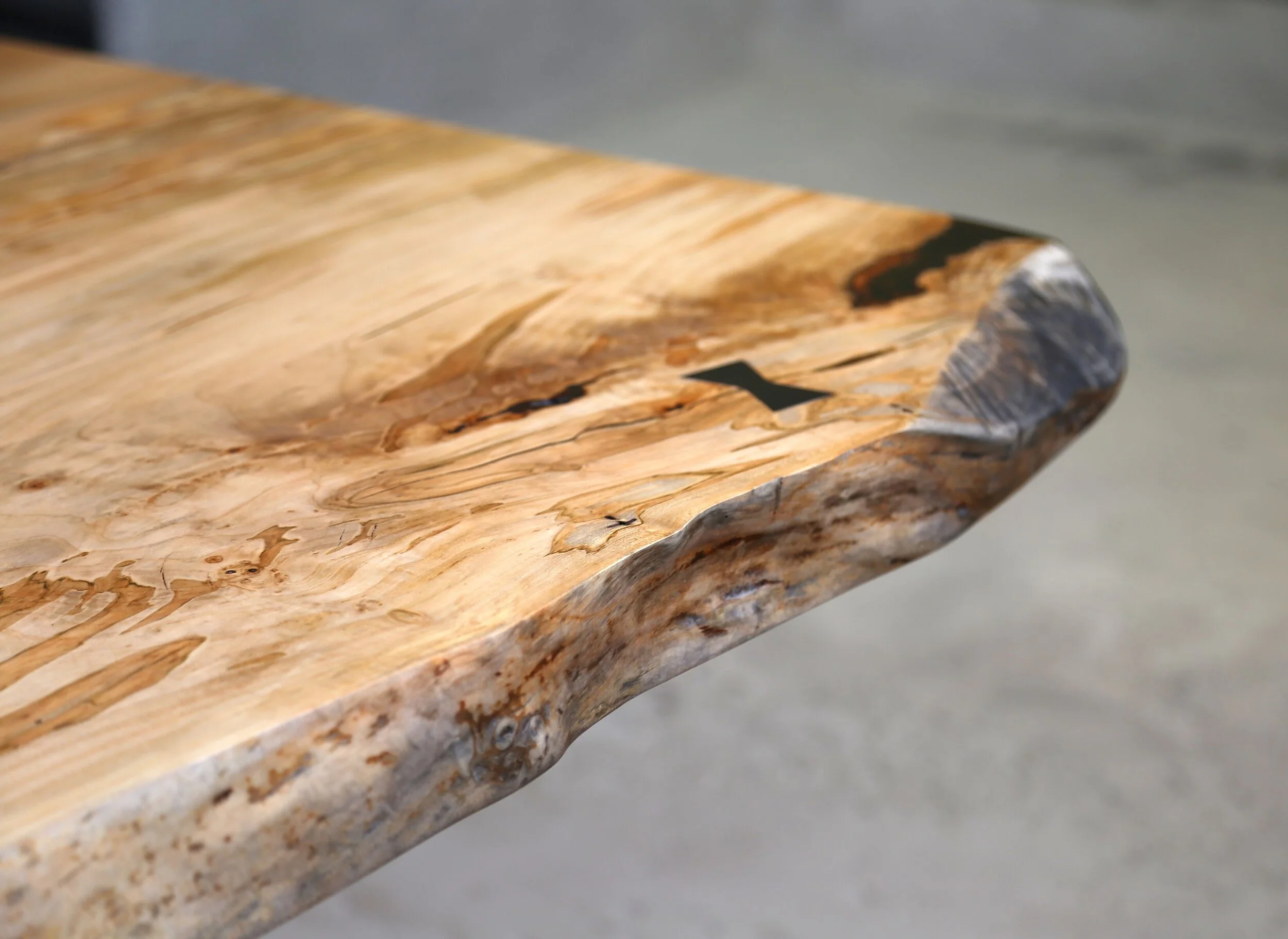 A Detail Of A SENTIENT Signature Live Edge Table In Ambrosia Maple With A Blackened Steel Butterly Inlay